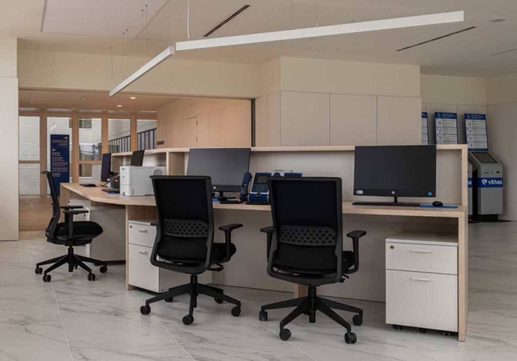 Zona de recepció d'oficina amb taulers de treball, cadires ergonòmiques negres i bucs de calaixos blancs